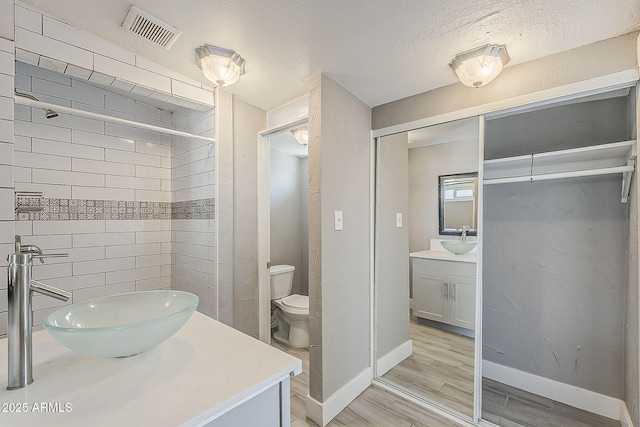 bathroom featuring vanity, baseboards, wood finished floors, toilet, and a textured ceiling