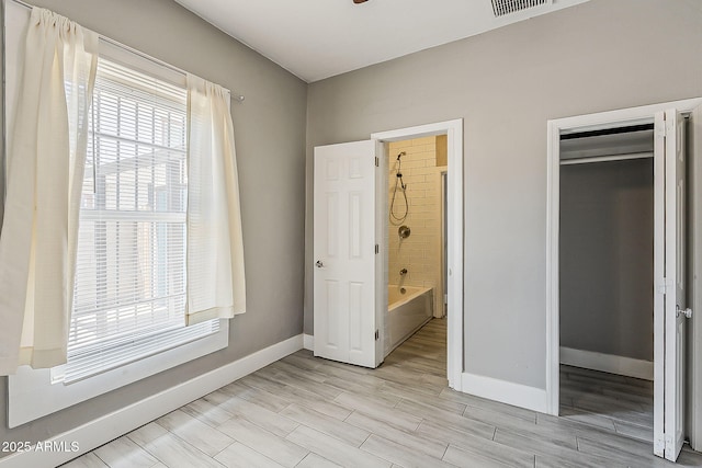 unfurnished bedroom featuring baseboards, multiple windows, light wood finished floors, and ensuite bathroom