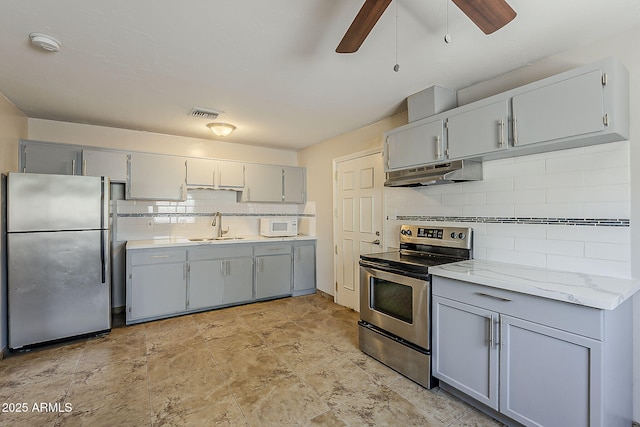 kitchen with stainless steel appliances, gray cabinets, under cabinet range hood, a ceiling fan, and a sink