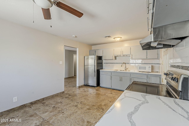 kitchen with freestanding refrigerator, a sink, ceiling fan, under cabinet range hood, and white microwave