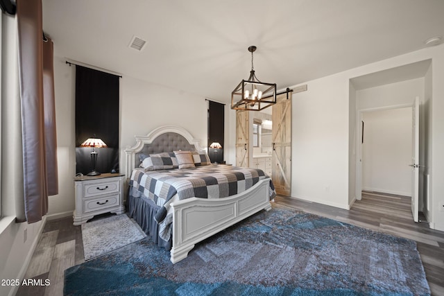 bedroom with dark hardwood / wood-style flooring, ensuite bath, a barn door, and an inviting chandelier