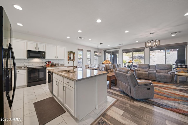 kitchen with sink, white cabinetry, black appliances, and a center island with sink