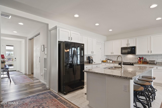 kitchen featuring white cabinetry, an island with sink, light stone counters, a breakfast bar, and black appliances