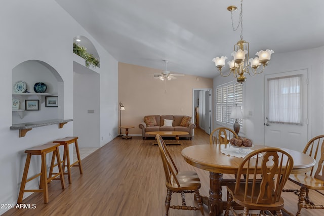 dining area featuring light hardwood / wood-style flooring, ceiling fan with notable chandelier, and vaulted ceiling