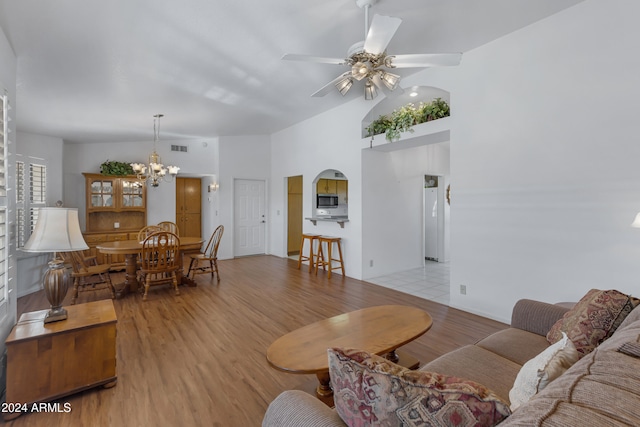 living room with ceiling fan with notable chandelier, light wood-type flooring, and vaulted ceiling