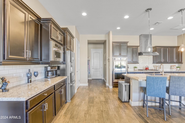 15201 S 183rd Dr, Goodyear, AZ 85338 - kitchen with light wood finished floors, light stone countertops, a kitchen bar, appliances with stainless steel finishes, and wall chimney range hood