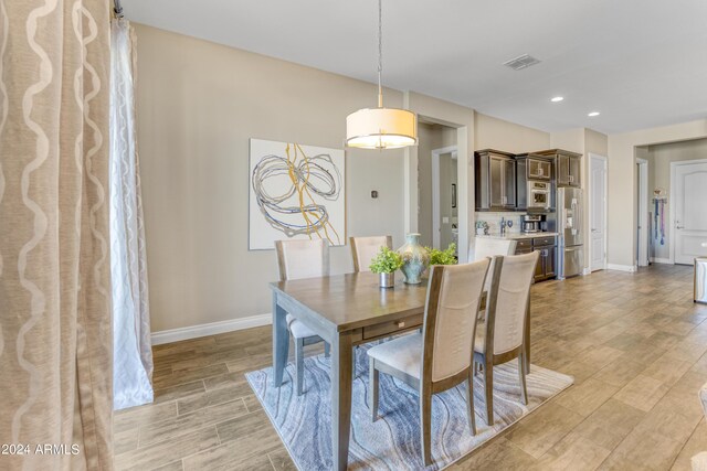 kitchen with tasteful backsplash, decorative light fixtures, light hardwood / wood-style flooring, wall chimney range hood, and appliances with stainless steel finishes