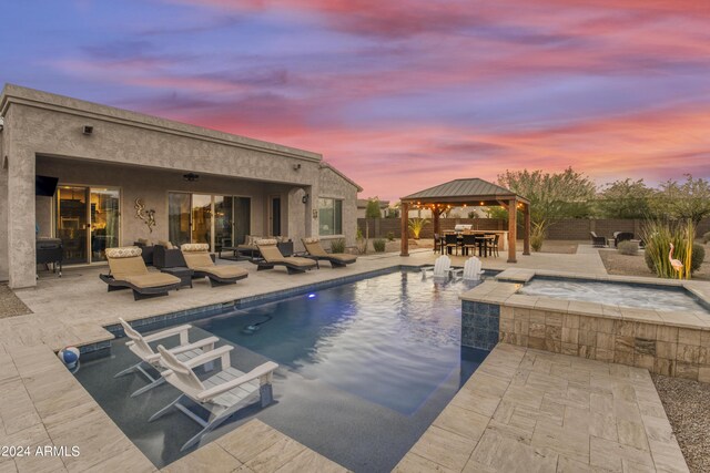 pool at dusk with a patio, an in ground hot tub, and a gazebo