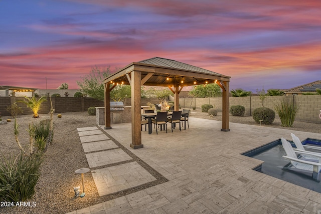 15201 S 183rd Dr, Goodyear, AZ 85338 - patio terrace at dusk featuring a fenced backyard, area for grilling, a gazebo, and outdoor dining space