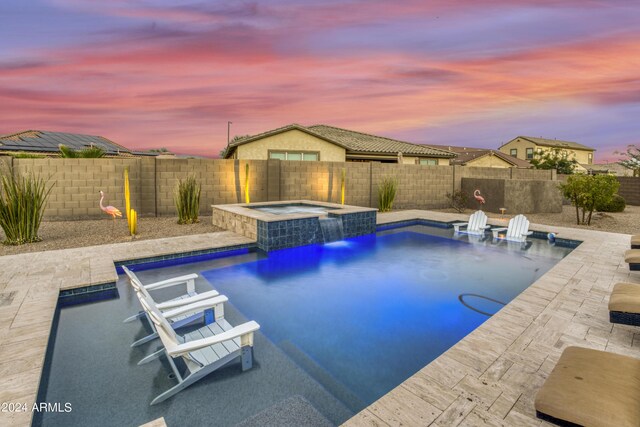 pool at dusk featuring pool water feature, a patio, and an in ground hot tub