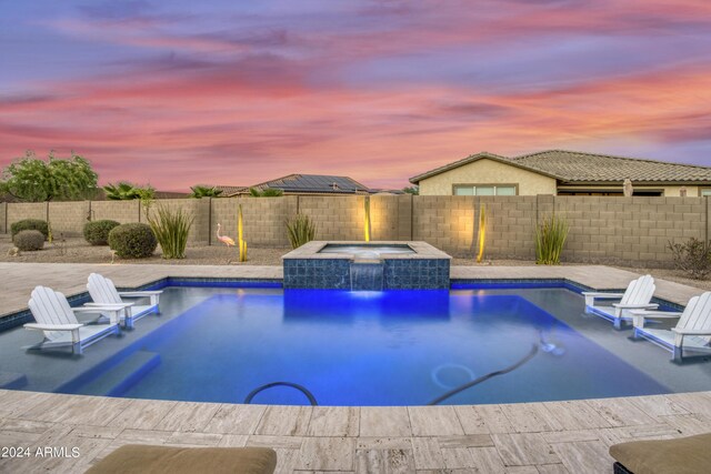 pool at dusk with pool water feature, an in ground hot tub, and a patio area