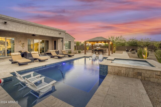 pool at dusk featuring a gazebo, an in ground hot tub, and a patio area