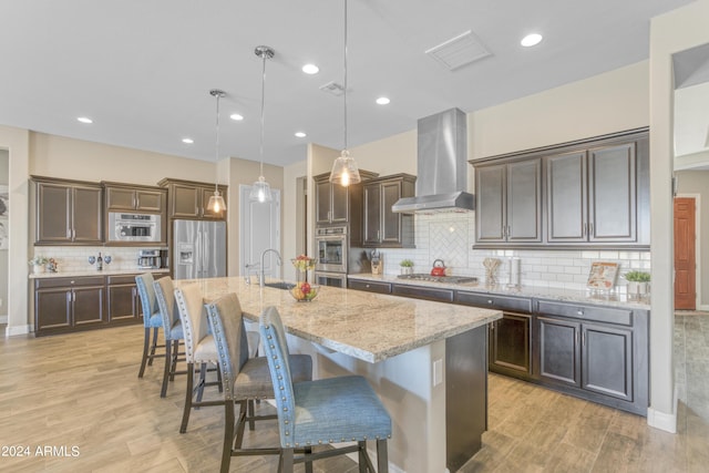 15201 S 183rd Dr, Goodyear, AZ 85338 - kitchen featuring stainless steel appliances, dark brown cabinetry, a sink, wall chimney range hood, and a kitchen breakfast bar