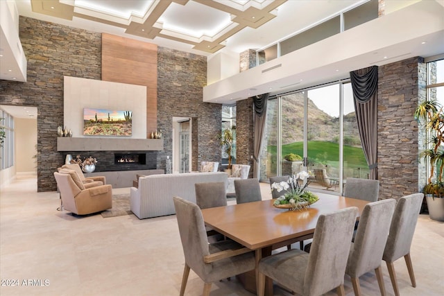 dining area featuring a fireplace, coffered ceiling, and a high ceiling