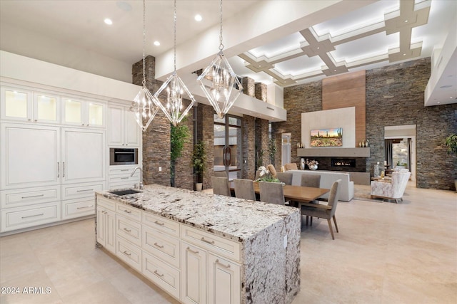 kitchen with light stone countertops, sink, pendant lighting, a high ceiling, and an island with sink