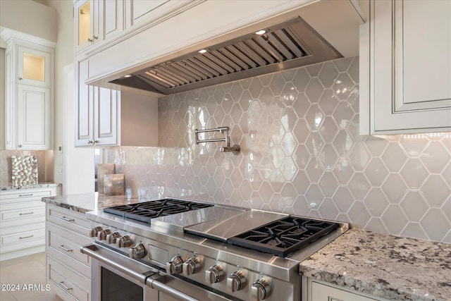 kitchen with decorative backsplash, custom range hood, stainless steel range, light stone counters, and white cabinetry