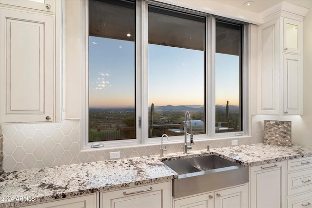 kitchen with backsplash, light stone countertops, white cabinetry, and sink