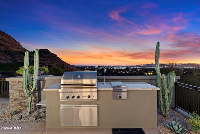 patio terrace at dusk featuring an outdoor kitchen, a mountain view, and grilling area