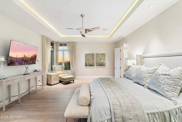 bedroom featuring a raised ceiling, ceiling fan, and light hardwood / wood-style flooring