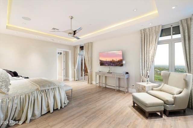 bedroom with ceiling fan, light hardwood / wood-style floors, and a raised ceiling