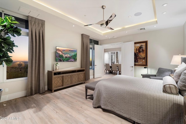 bedroom featuring ceiling fan, light hardwood / wood-style floors, and a tray ceiling