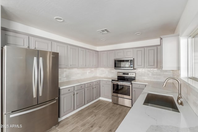 kitchen featuring stainless steel appliances, tasteful backsplash, light wood-style flooring, a sink, and light stone countertops