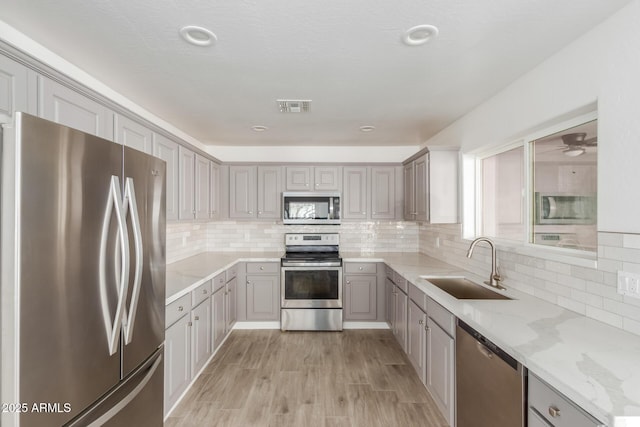 kitchen featuring visible vents, stainless steel appliances, a sink, and gray cabinetry