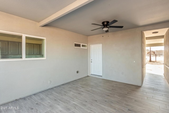 empty room featuring a ceiling fan, light wood-type flooring, and beamed ceiling