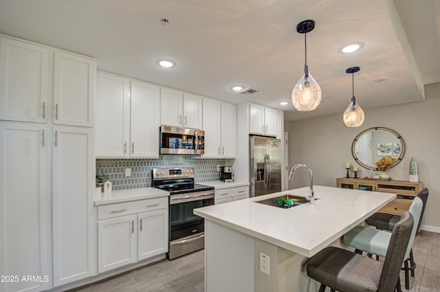 kitchen featuring sink, white cabinetry, an island with sink, hanging light fixtures, and appliances with stainless steel finishes