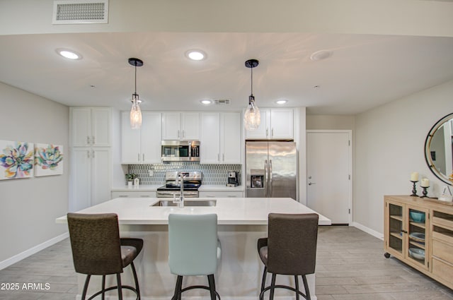 kitchen with a center island with sink, hanging light fixtures, and appliances with stainless steel finishes