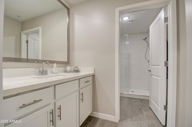 bathroom with hardwood / wood-style flooring, a tile shower, and vanity