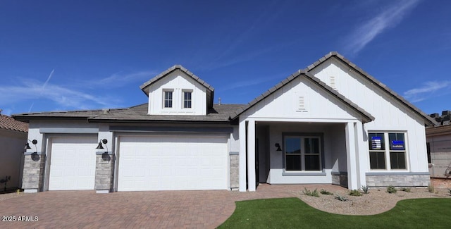 view of front facade featuring stone siding, decorative driveway, an attached garage, and board and batten siding
