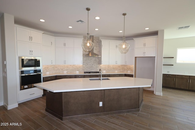 kitchen with appliances with stainless steel finishes, wall chimney exhaust hood, dark wood-style flooring, a sink, and white cabinets