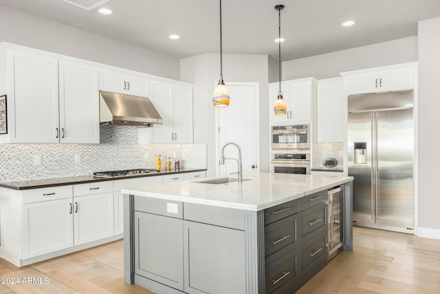 kitchen featuring sink, ventilation hood, pendant lighting, white cabinets, and appliances with stainless steel finishes