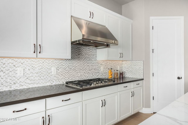 kitchen with white cabinetry, stainless steel gas cooktop, light hardwood / wood-style flooring, backsplash, and dark stone counters