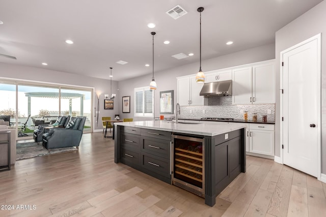 kitchen featuring wine cooler, pendant lighting, a kitchen island with sink, white cabinets, and light wood-type flooring