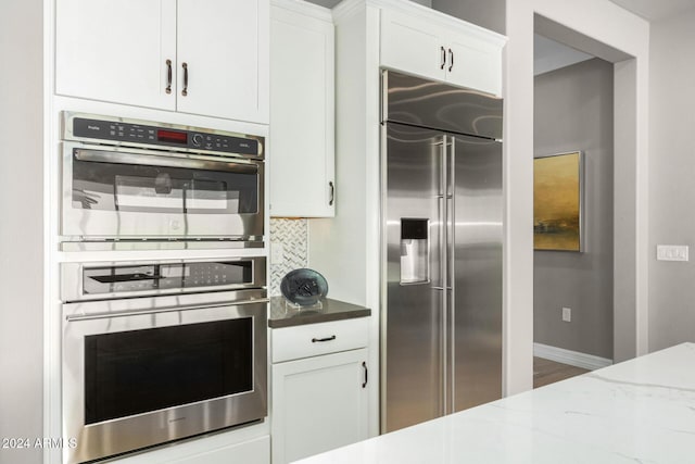 kitchen featuring white cabinets, backsplash, light stone counters, and stainless steel appliances