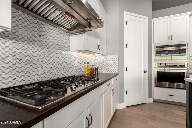 kitchen featuring backsplash, white cabinets, light hardwood / wood-style flooring, wall chimney exhaust hood, and stainless steel appliances