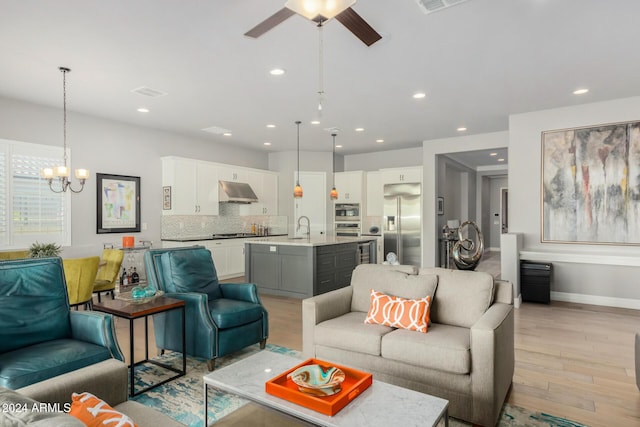 living room with ceiling fan with notable chandelier, light hardwood / wood-style flooring, and sink