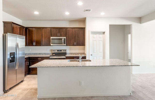 kitchen featuring stainless steel appliances, sink, light stone counters, and an island with sink