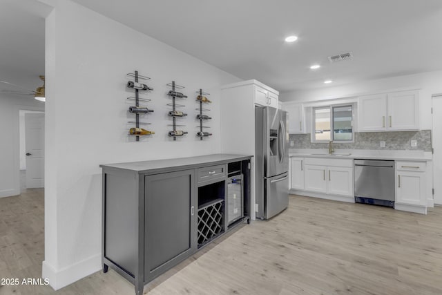 kitchen featuring appliances with stainless steel finishes, light wood finished floors, a sink, white cabinets, and recessed lighting