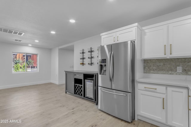 kitchen featuring stainless steel fridge with ice dispenser, light countertops, white cabinets, light wood-type flooring, and backsplash