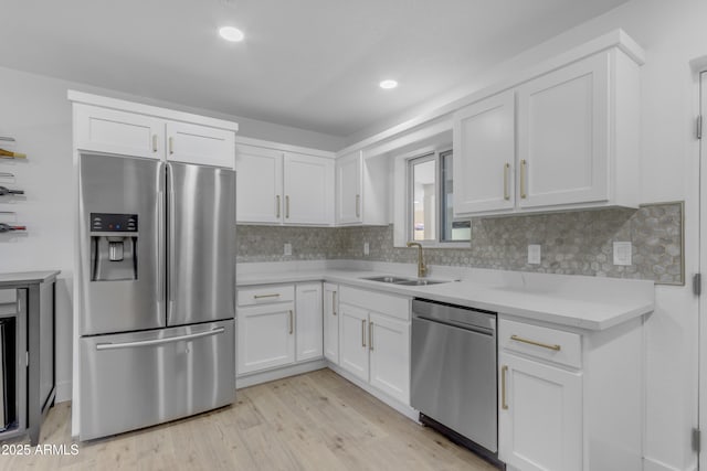 kitchen with appliances with stainless steel finishes, a sink, light wood finished floors, white cabinetry, and tasteful backsplash