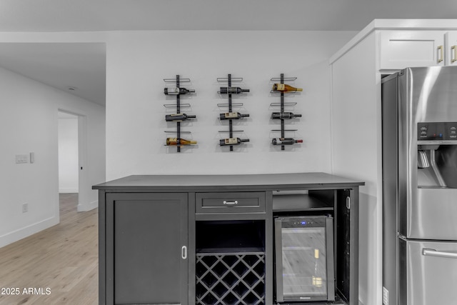 bar featuring stainless steel fridge with ice dispenser, wine cooler, light wood-style flooring, and baseboards