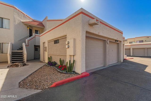 view of side of home with driveway, a tiled roof, an attached garage, stairs, and stucco siding