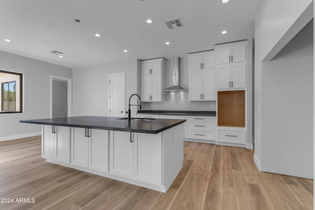 kitchen with a large island with sink, white cabinetry, sink, and wall chimney range hood