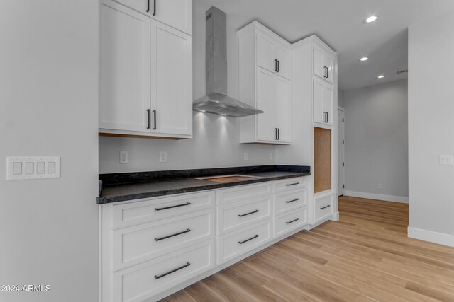 kitchen featuring cooktop, light hardwood / wood-style flooring, white cabinets, and wall chimney exhaust hood