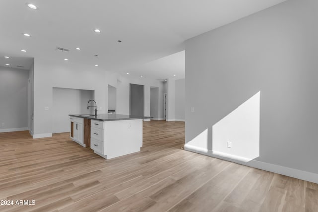 kitchen with an island with sink, sink, white cabinets, and light wood-type flooring