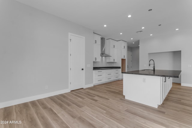 kitchen featuring wall chimney exhaust hood, sink, white cabinetry, a center island with sink, and a kitchen breakfast bar