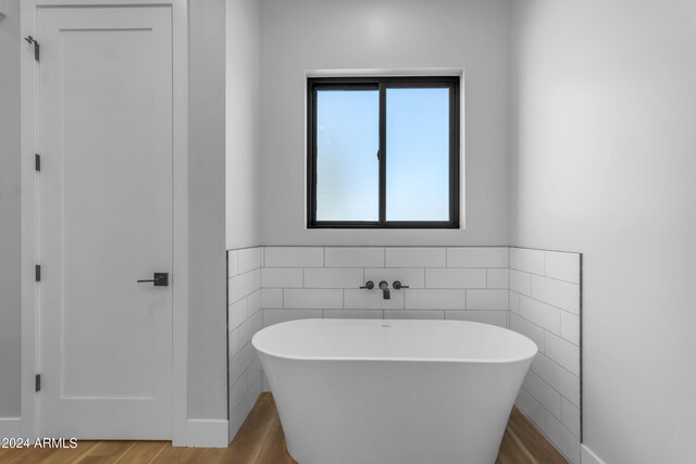 bathroom with wood-type flooring, a washtub, and tile walls